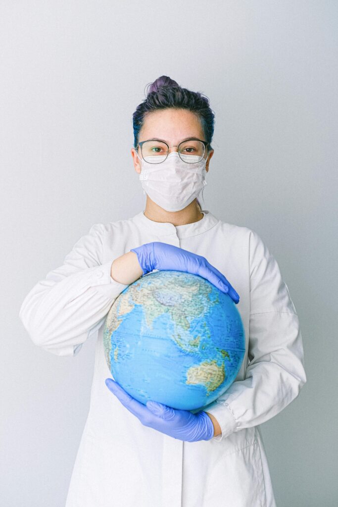 A medical professional wearing a mask and gloves holds a globe, symbolizing global health care during a pandemic.